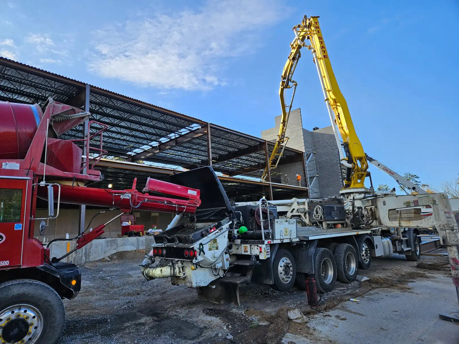 Boom pump and mixer trucks set up for an elevated deck pour inside a steel-framed building
