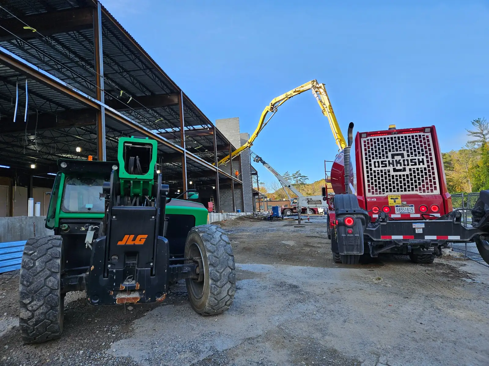 Telehandler and concrete pump working inside a steel structure on a commercial site