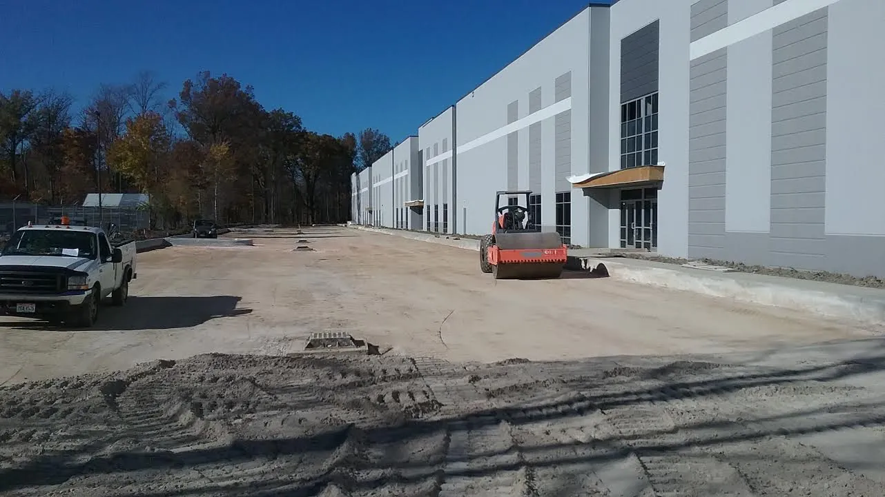 Roller compacting subgrade alongside a commercial warehouse before concrete placement